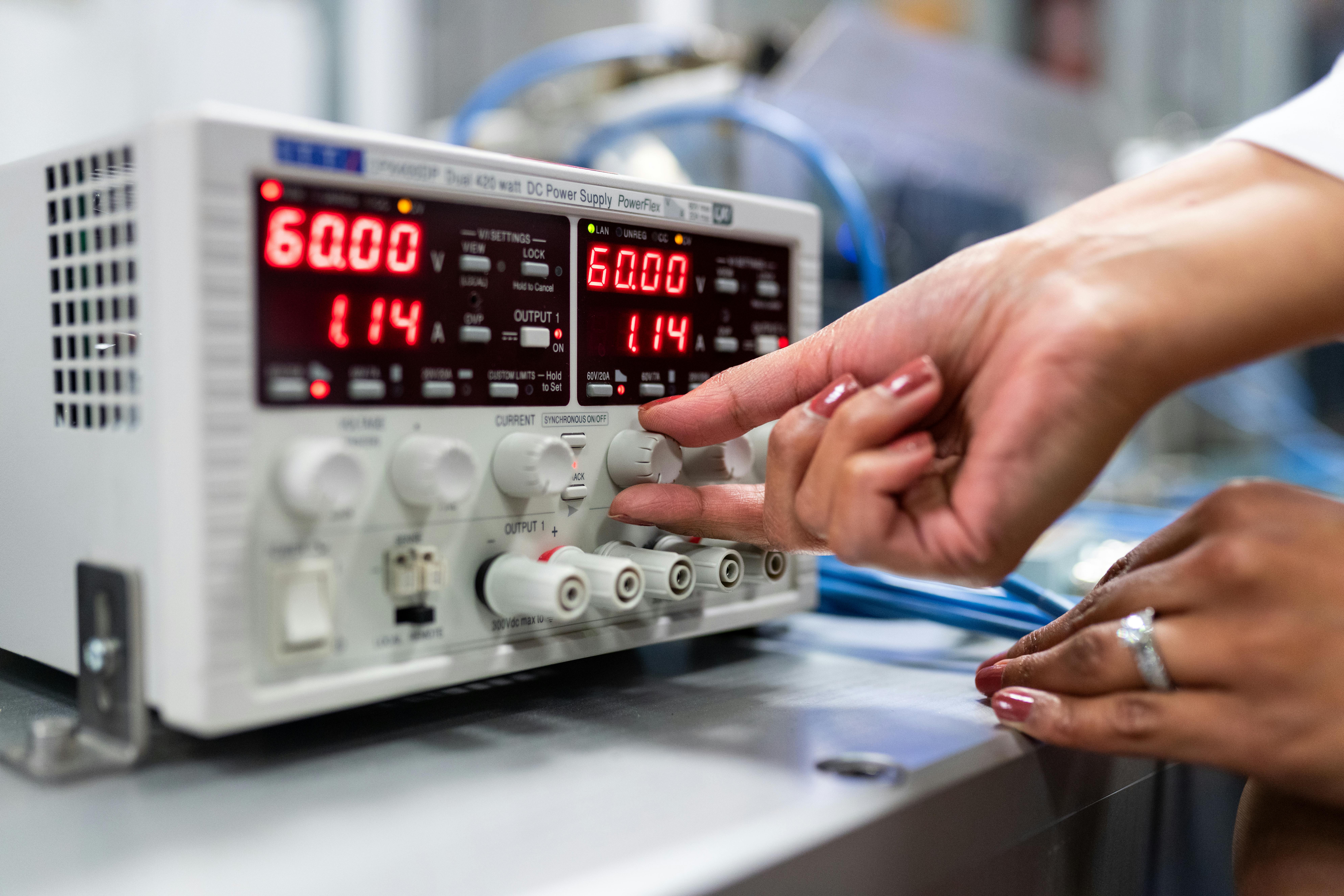 Close-up of a woman adjusting a DC power supply in a lab setting, indicating a hands-on approach to scientific research.