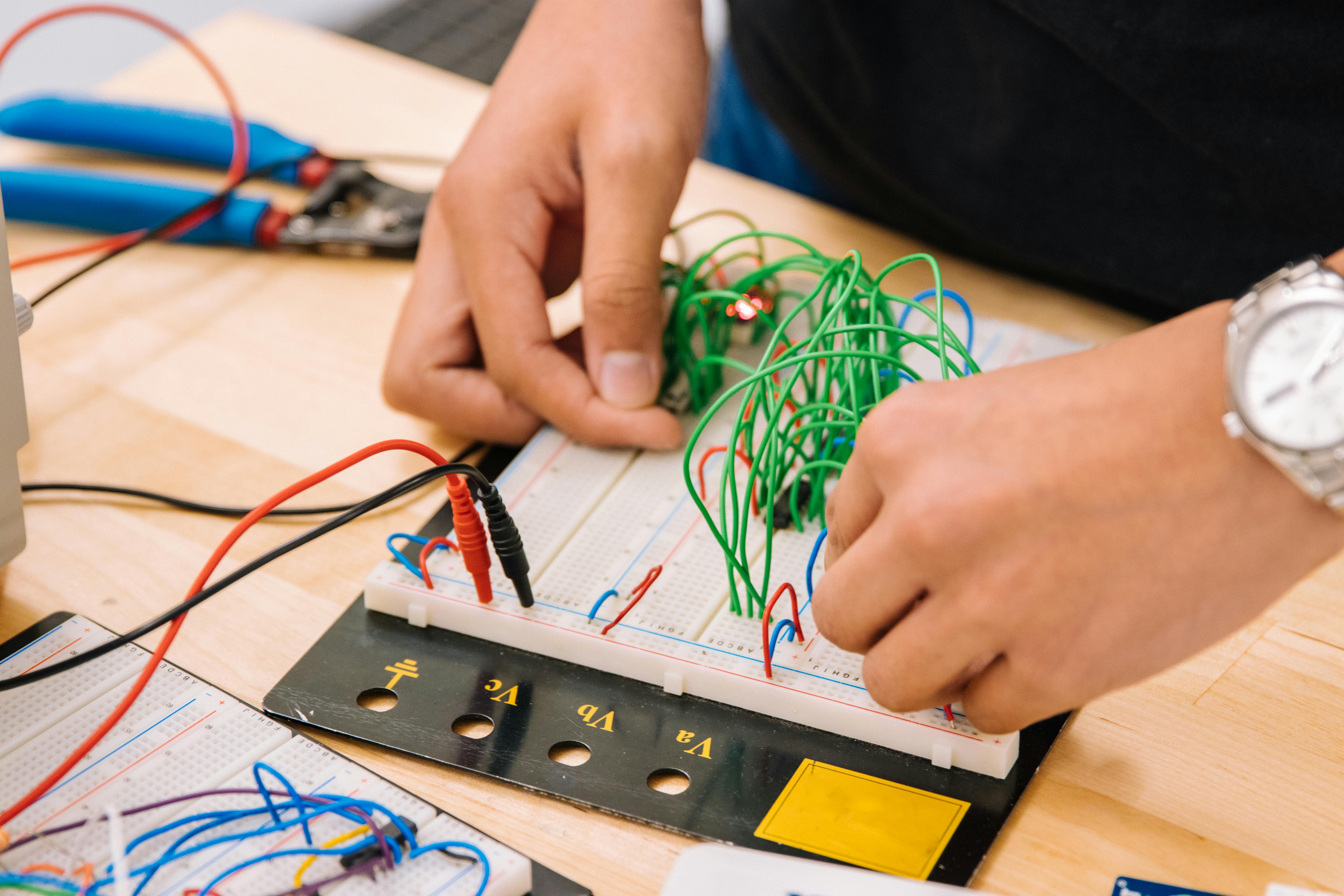 Close-up of hands working on electronic project with wires and breadboard.
